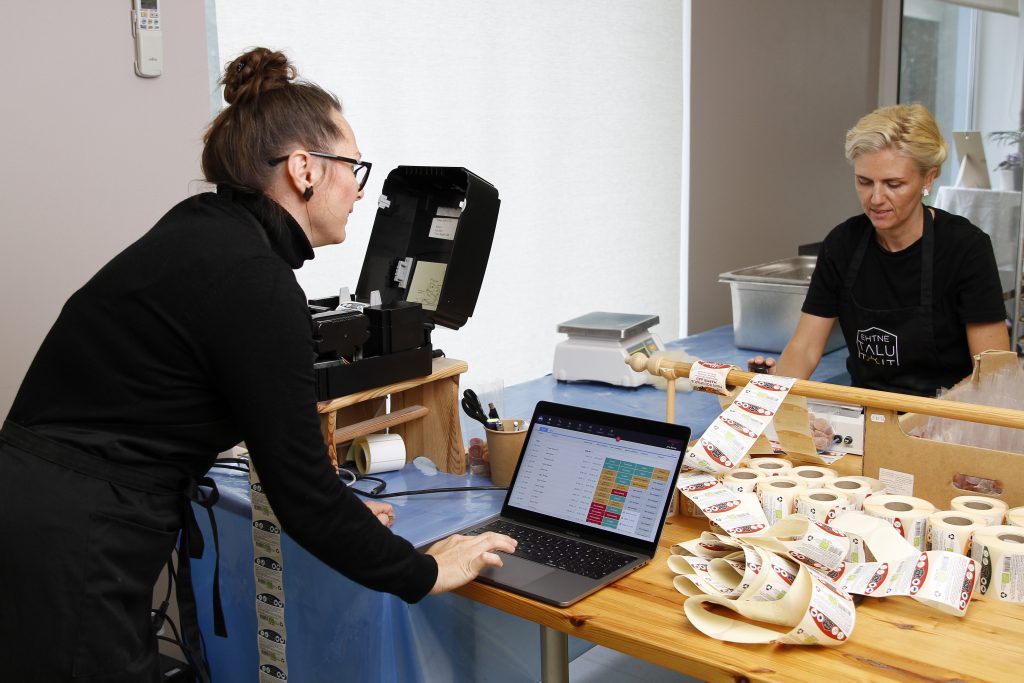 Two workers labeling candy final products while using a product traceability system at the workstation.
