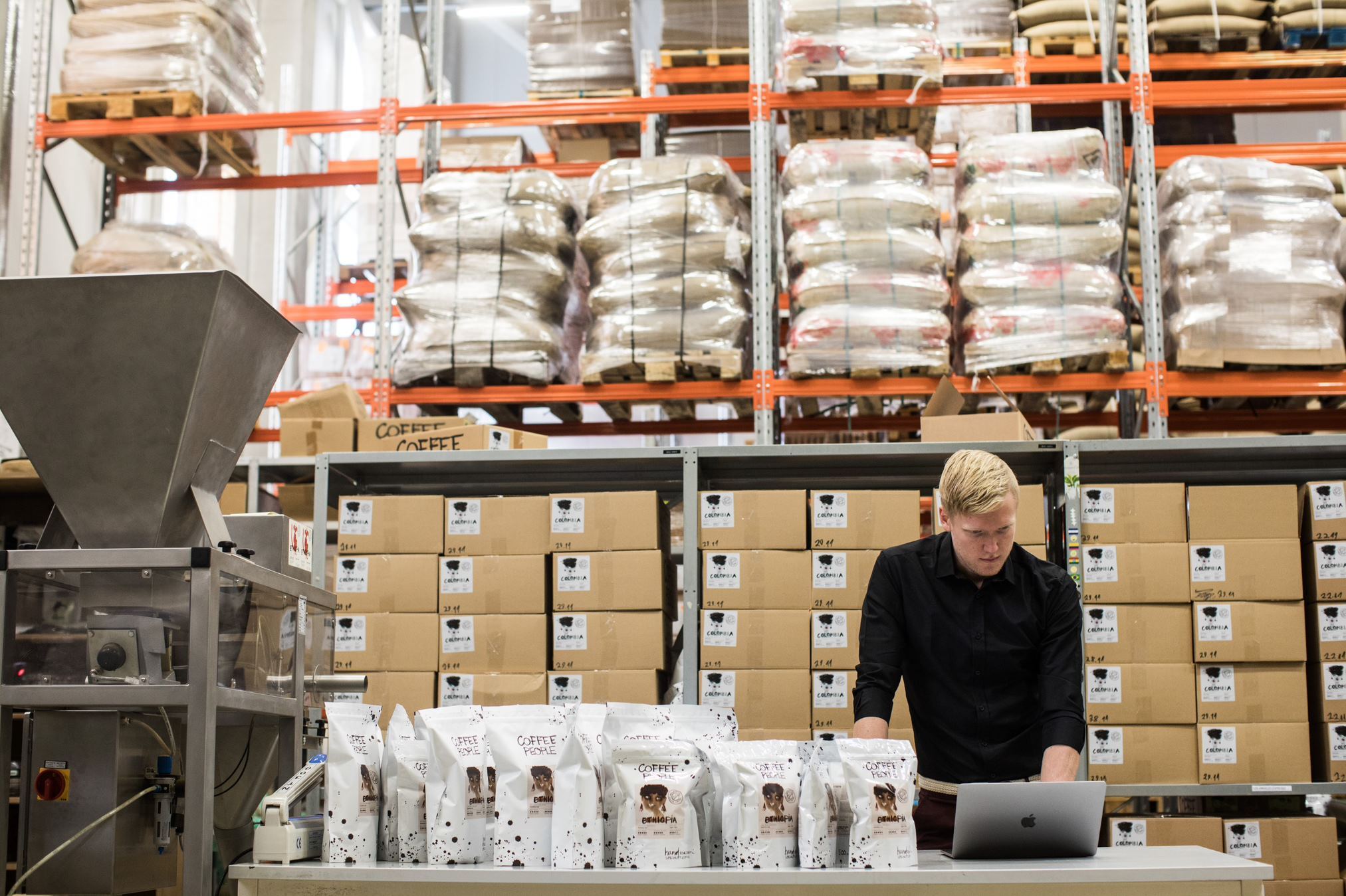 Coffee roaster stood in a warehouse, filled with inventory and equipment, updating their Shopify variant limit on their Katana ERP software.