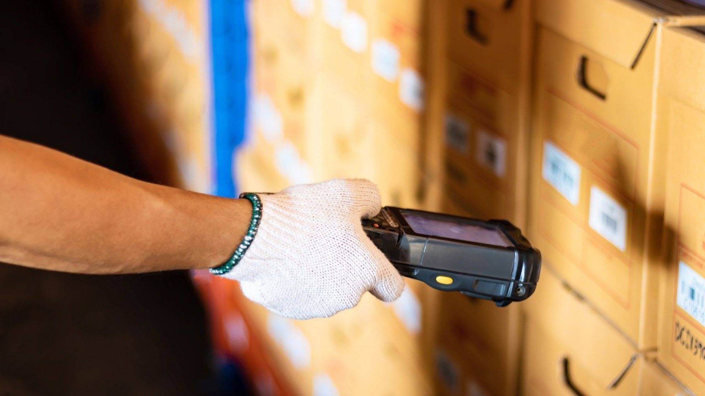 A hand holding barcode scanner and scanning barcode on a box