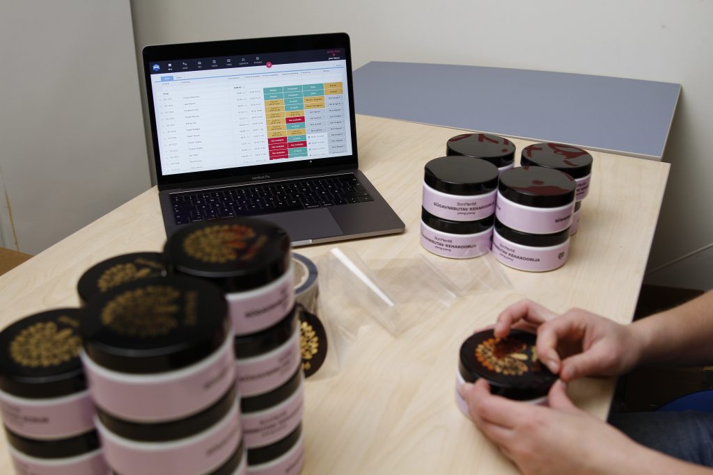 Cosmetics manufacturer labeling finished goods with Katana ERP software open on a laptop nearby. 