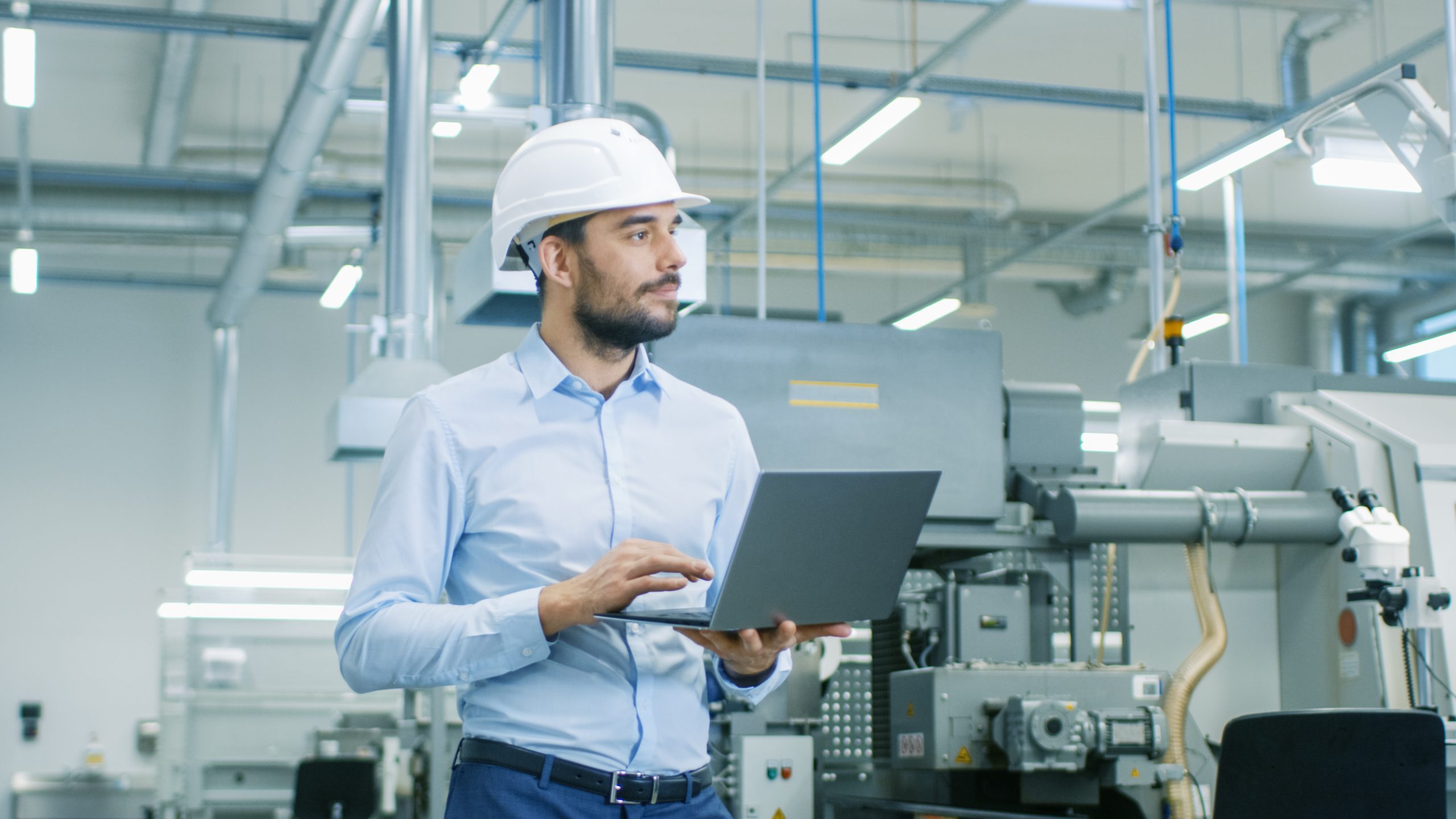 Manager wearing a hardhat in a sterile factory checking their master production schedule on a laptop.