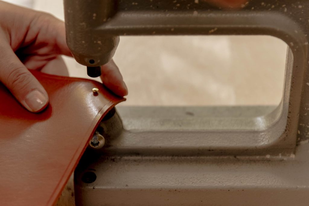close-up of a person piercing a leather sheet with a machine