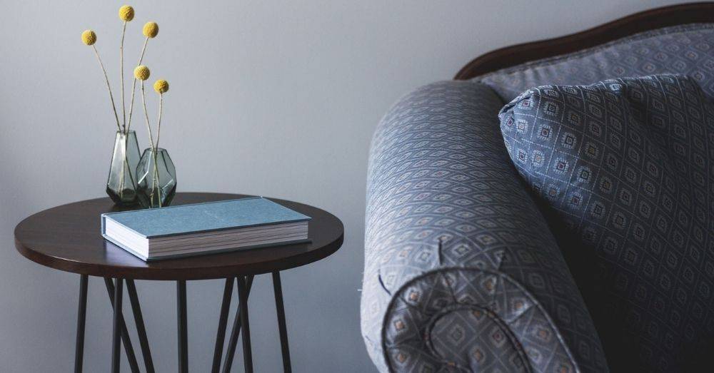 Furniture in a living room, a sofa, a table stand, and a book, representing the article about best Shopify furniture stores.