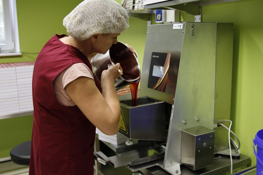 Candymaker pouring mixture into a machine on a shop floor. 