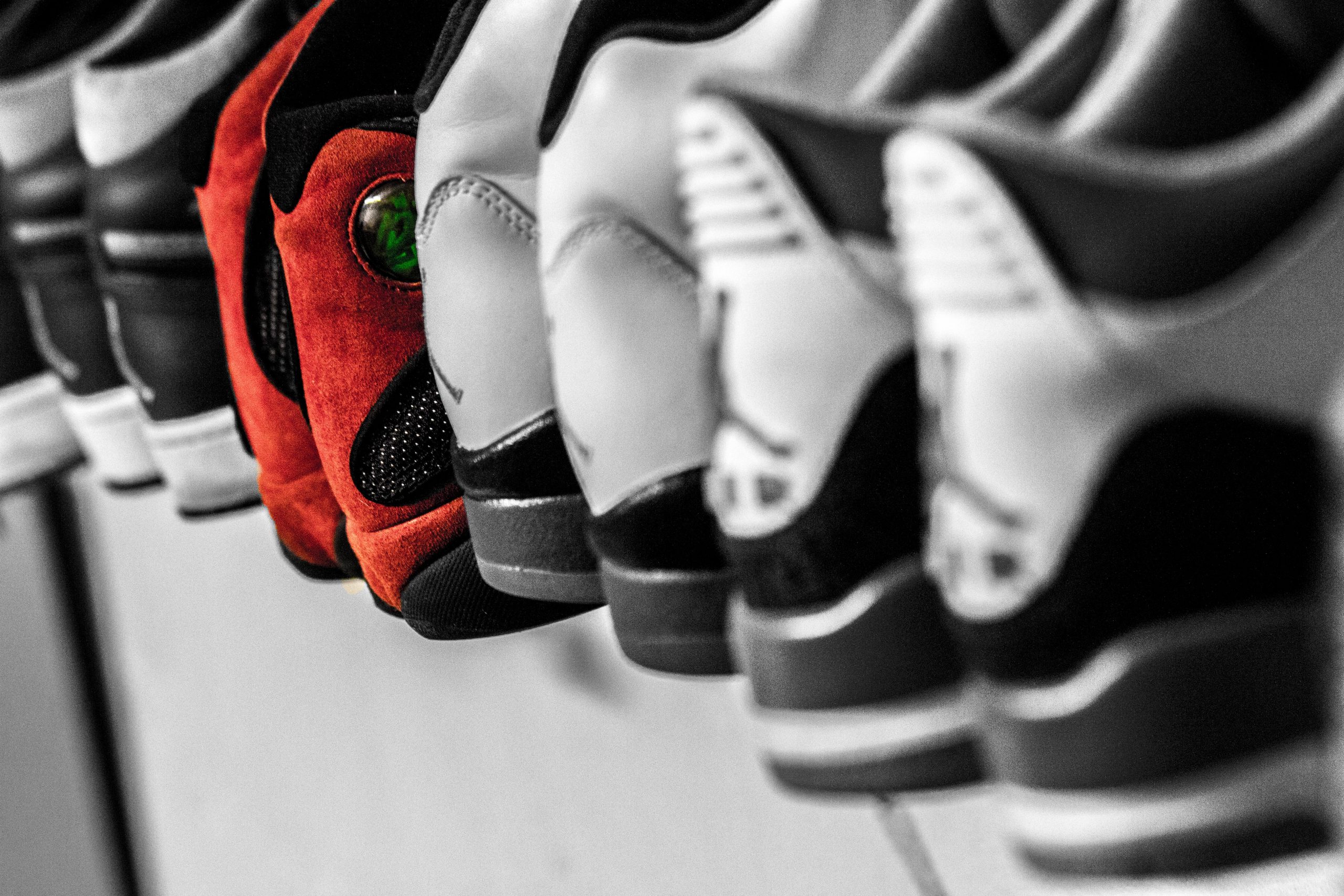 A collection of white sneakers with a pair of red sneakers in the middle of the shelf.