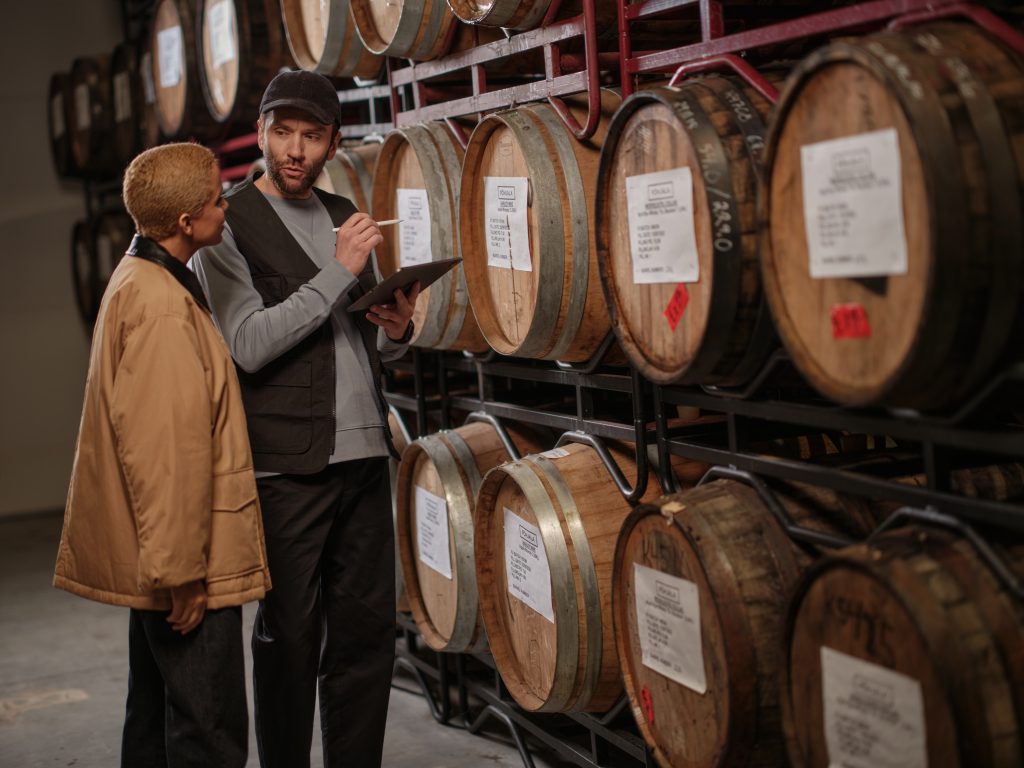 Two workers discussing processes in front of beer barrels