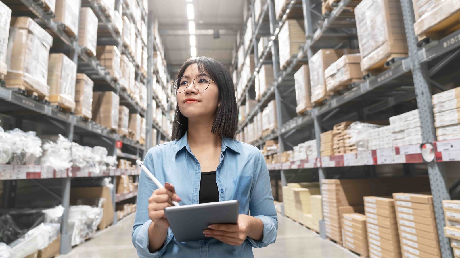 Woman with glasses in a warehouse holding a tablet