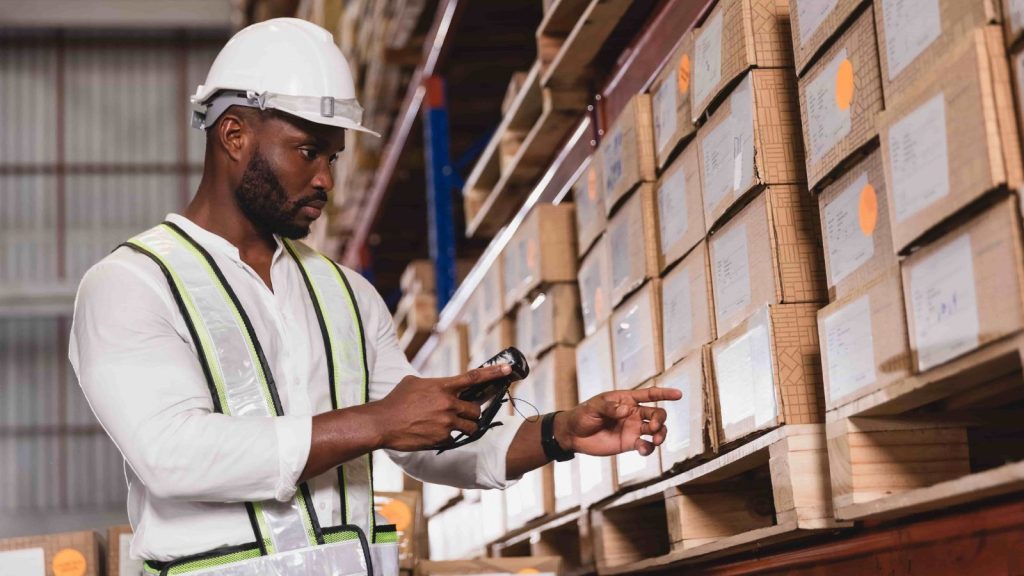 A worker with a handheld device scanning boxes on a warehouse shelf