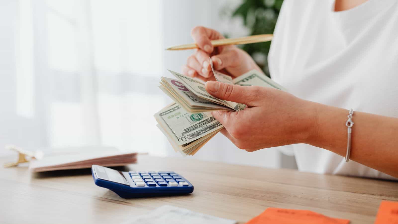 A person sitting at a desk counting dollar bills in their hand