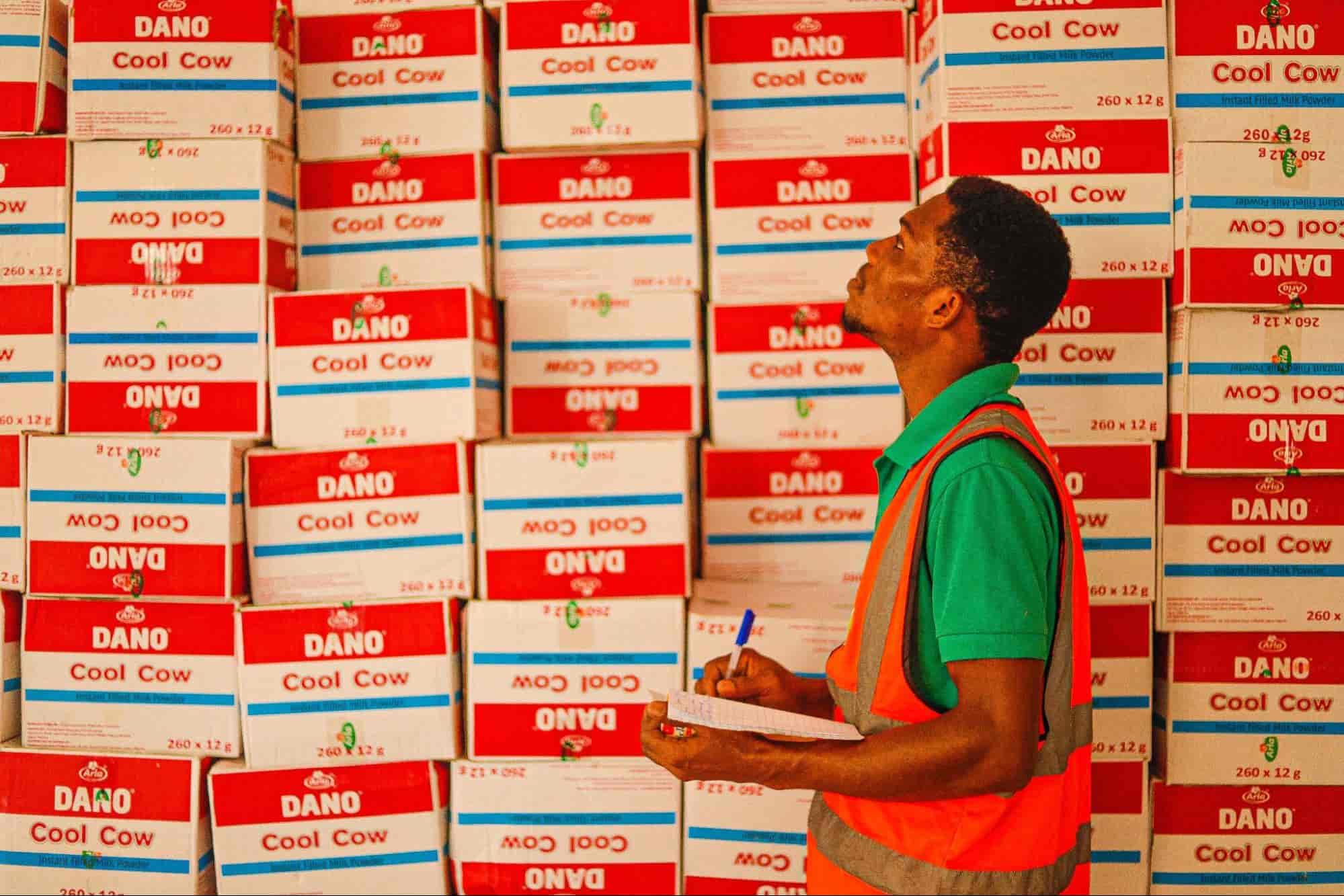 Man stood in front of wall of boxes updating a spreadhseet with a pen. 