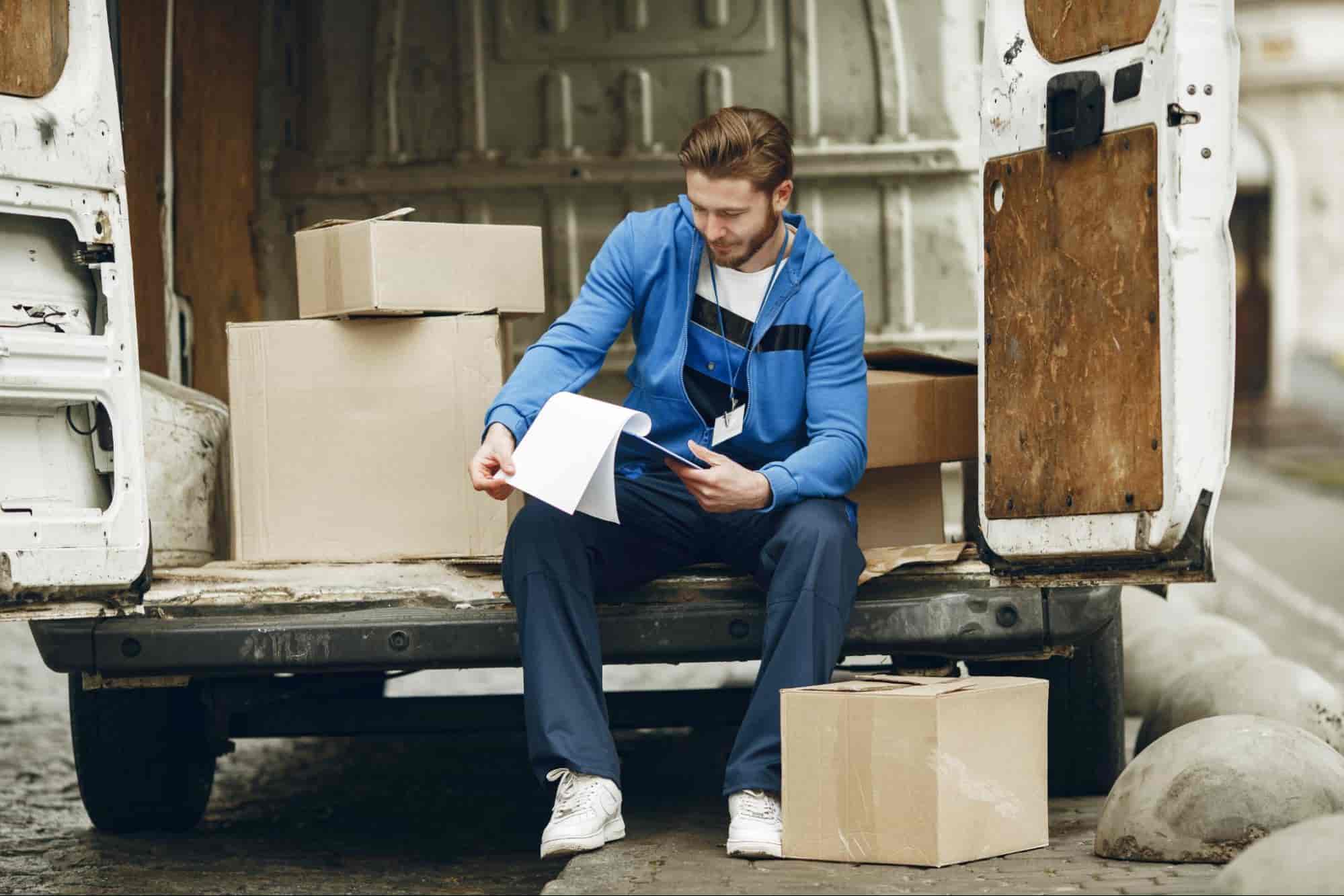 A man sat in a van with a supply chain issue, surrounded by inventory and looking through documents.