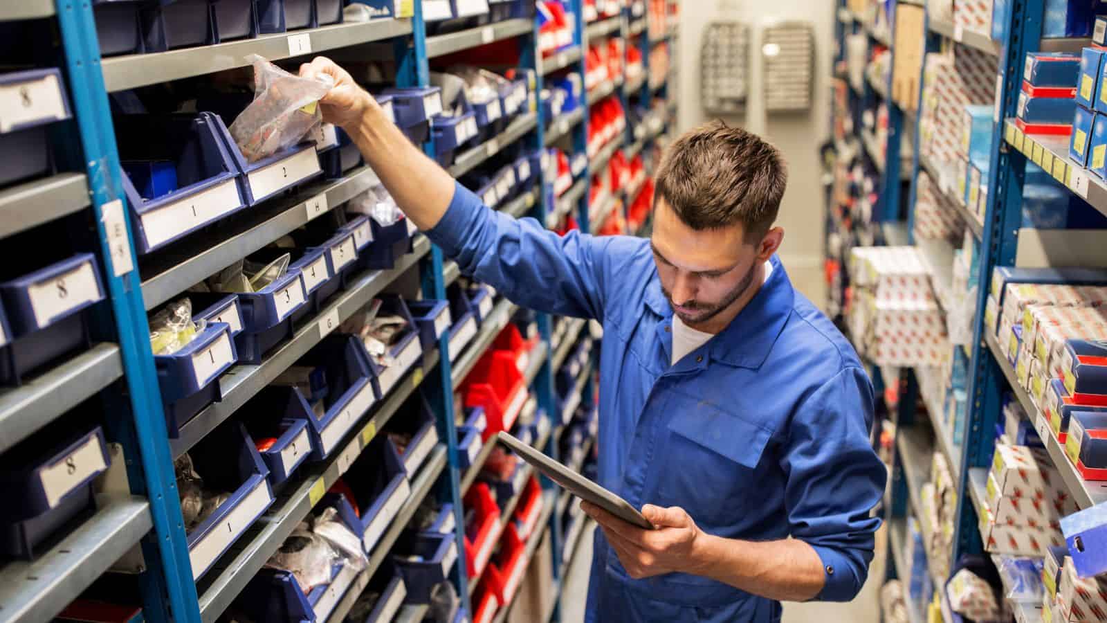 A man searching through his finished goods inventory, holding a smart device in his warehouse