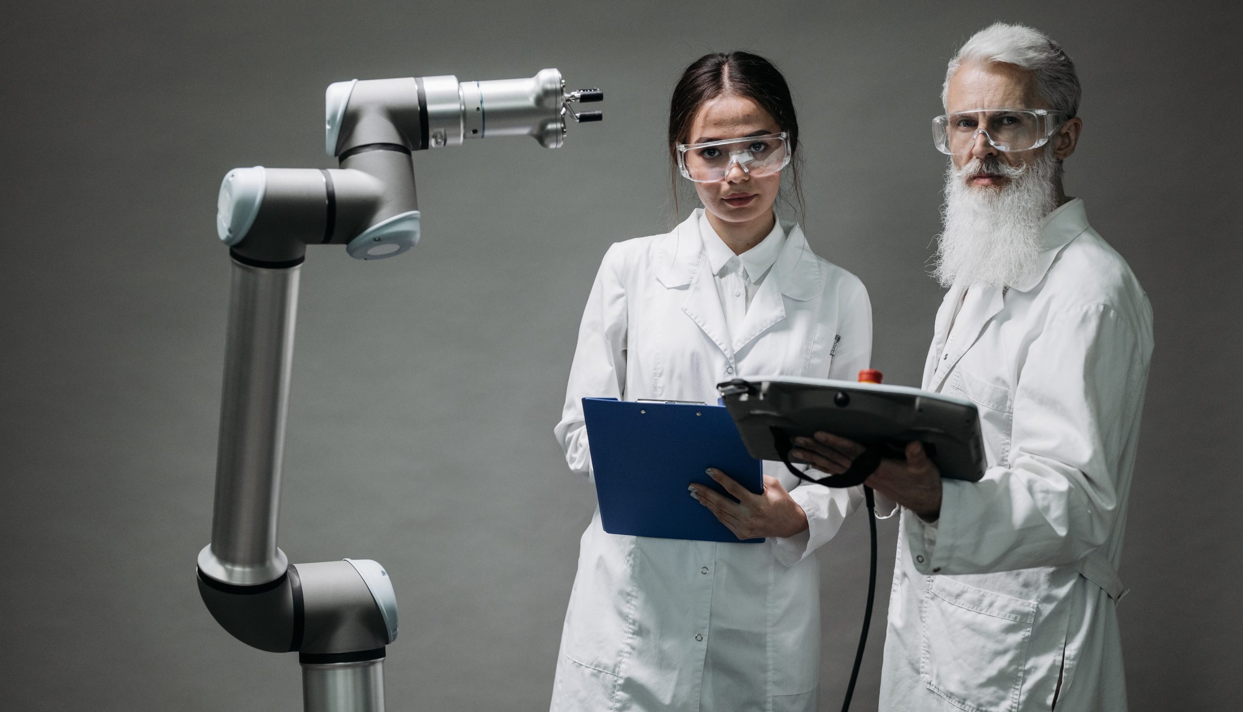 Two engineers with lab coats next to a robotic arm