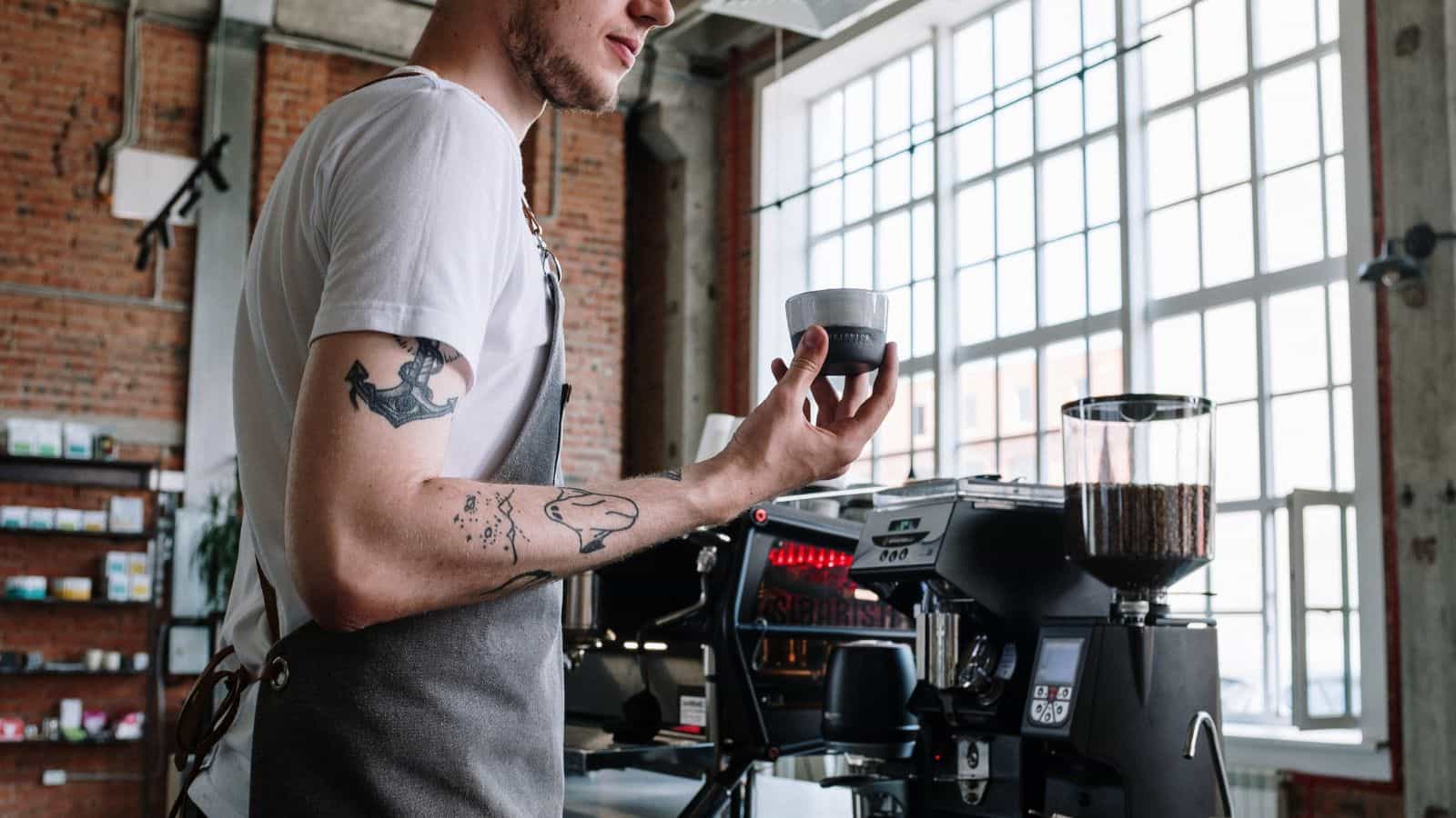 Barista holding an espresso cup in front of a coffee maker