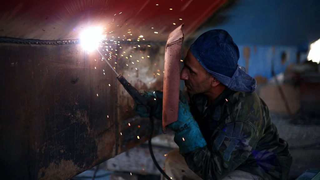 A man covers his eyes with a shield as he welds together some machinery.