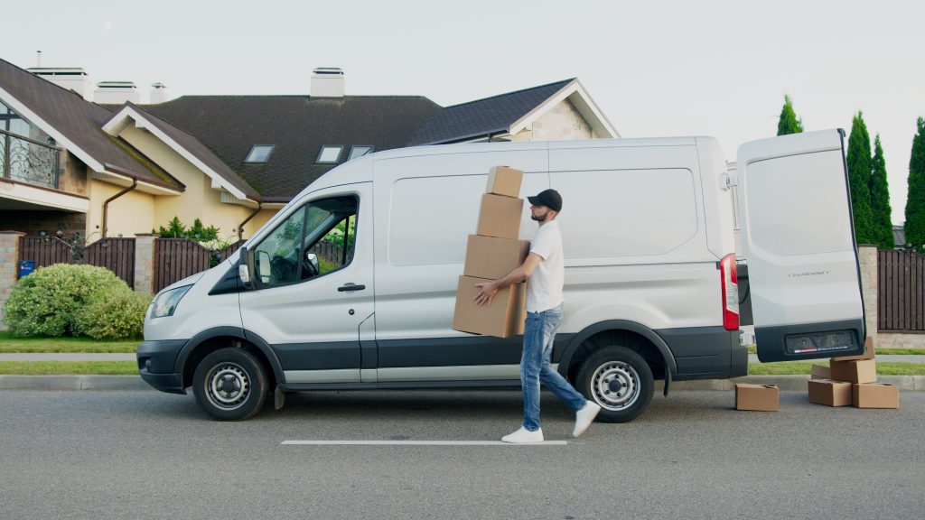 Delivery man carrying four boxes from his white van to the customer