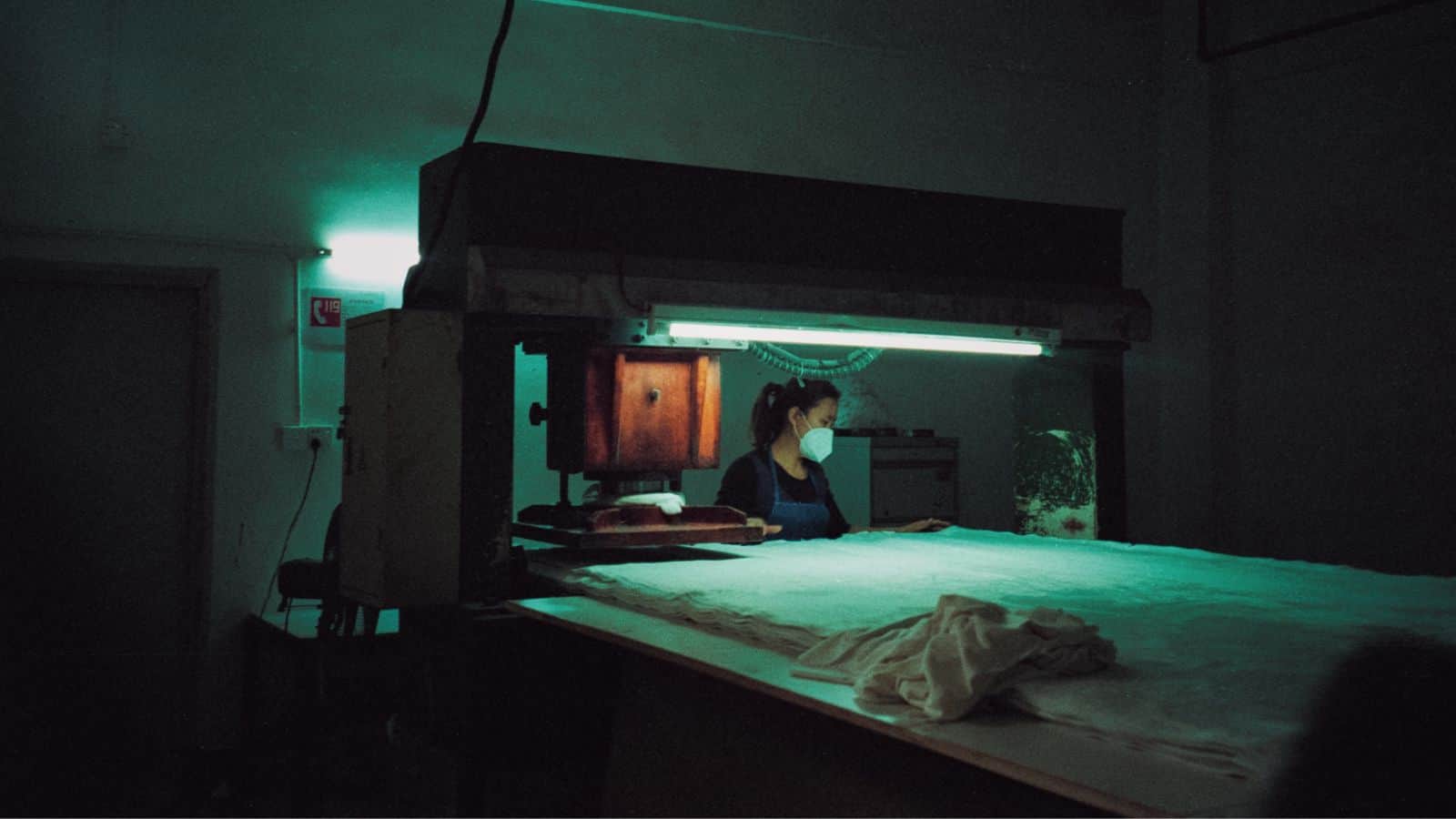 A female worker handling material while wearing a mask and PPE in manufacturing.