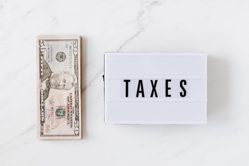 A stack of 50-dollar bills on a white stone tabletop with a box labeled taxes next to it