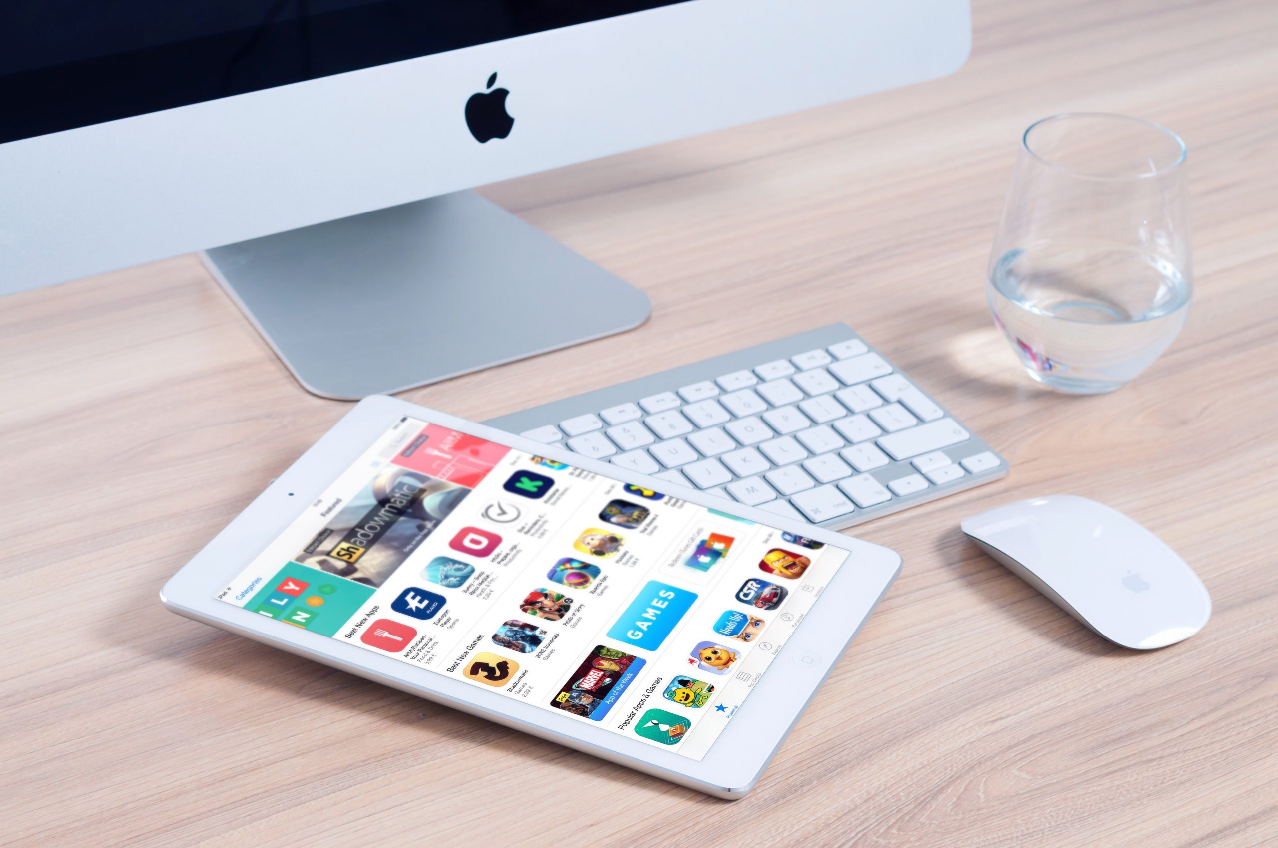 iMac on a desk with iPad laying on the keyboard showing the app store