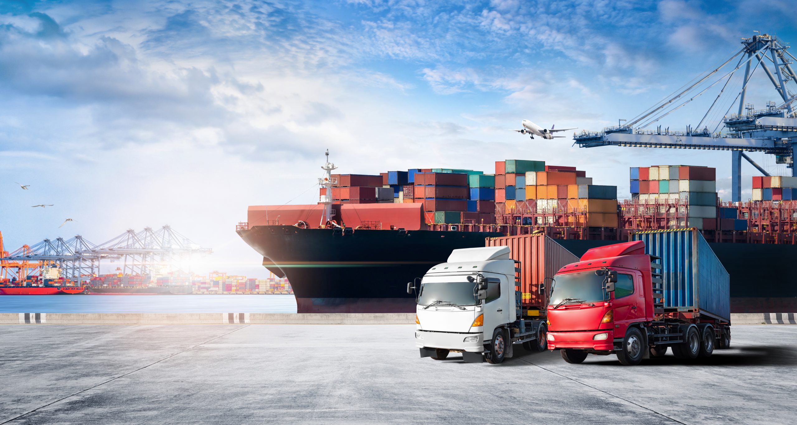 Two trucks parked in a port with a cargo ship parked in the dock