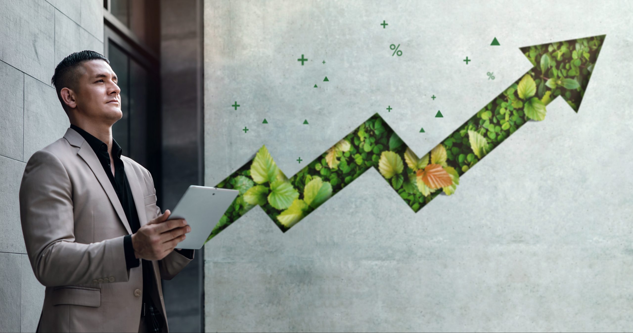 Man with a clipboard standing in front of a concrete wall with green plants growing inside the wall.