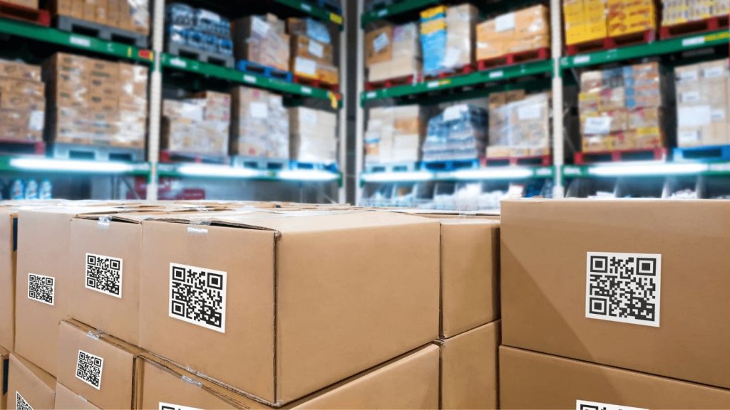 Boxes in a manufacturer's storage with QR codes, surrounded by shelves of inventory.
