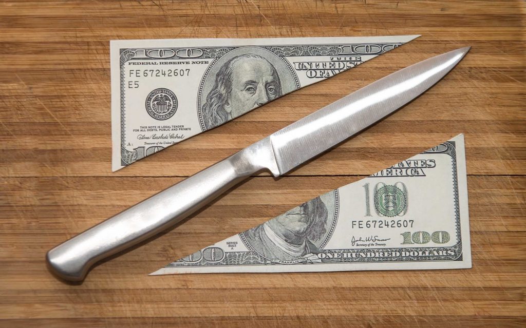 Knife sitting on a table next to a sliced 100 dollar bill
