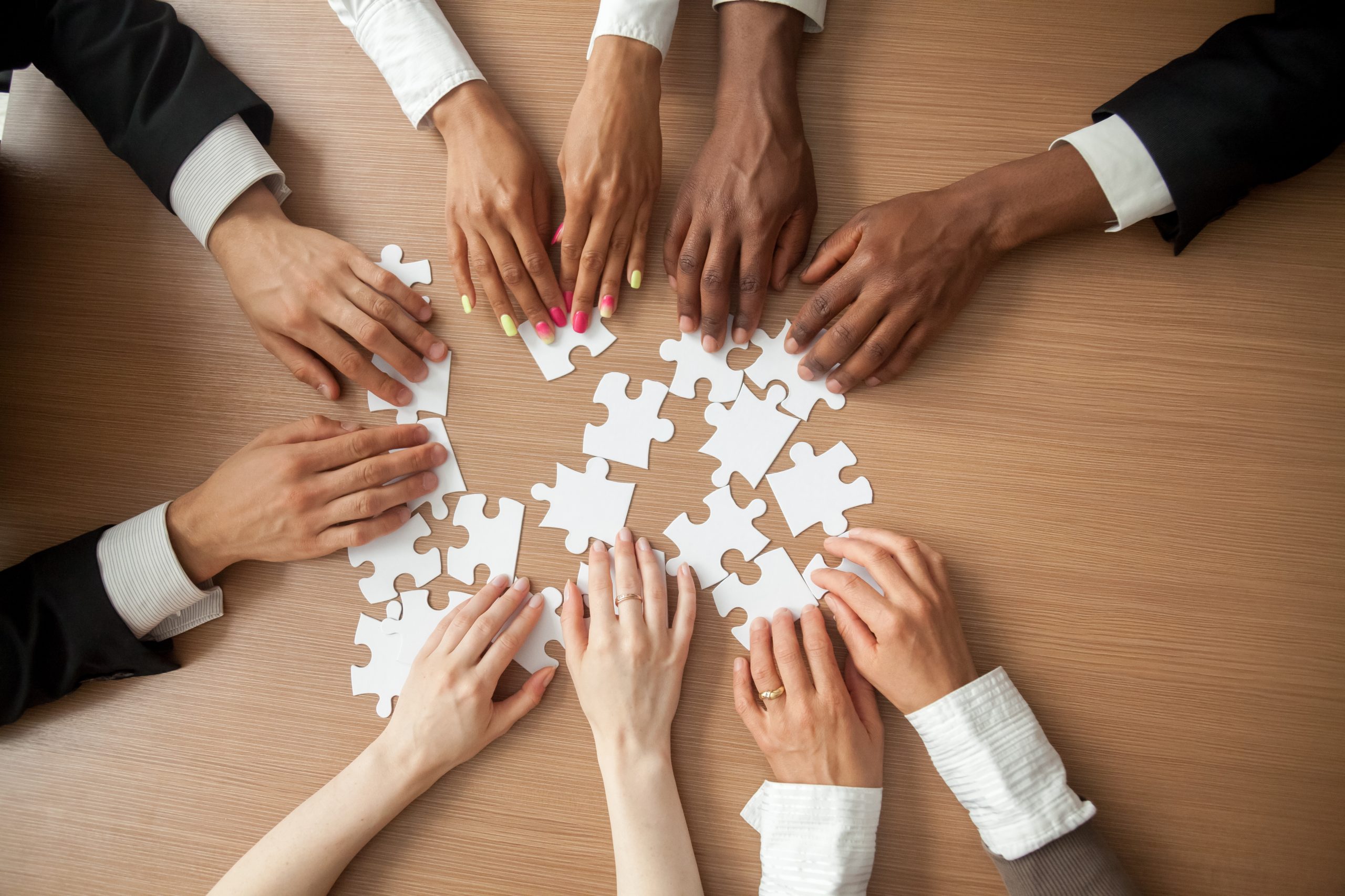 Multiple workers around a desk putting together a white jigsaw puzzle