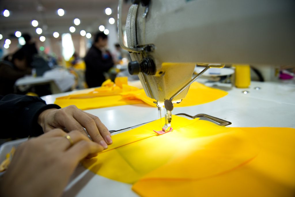 Person sewing a yellow piece of fabric in a clothing factory