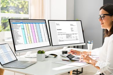 Accountant sitting behind her desk and looking at invoices and spreadsheets on her computer
