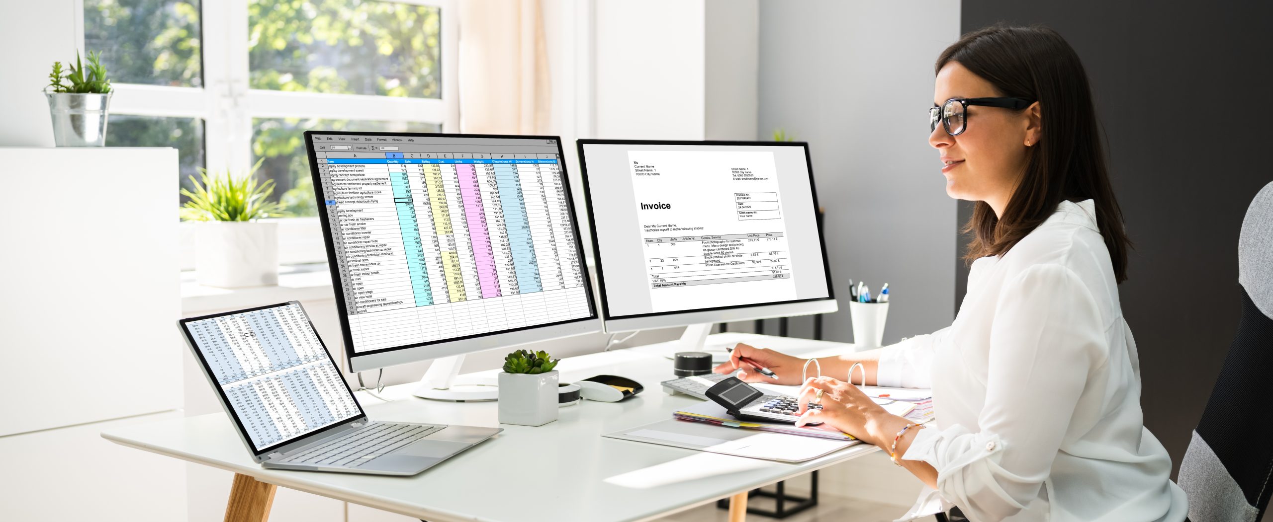 Accountant sitting behind her desk and looking at invoices and spreadsheets on her computer