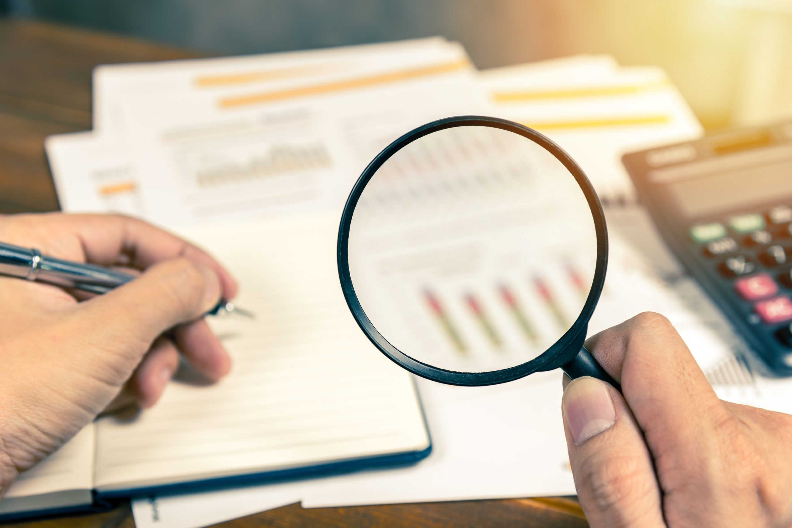 A person holding a magnifying glass looking at bar charts