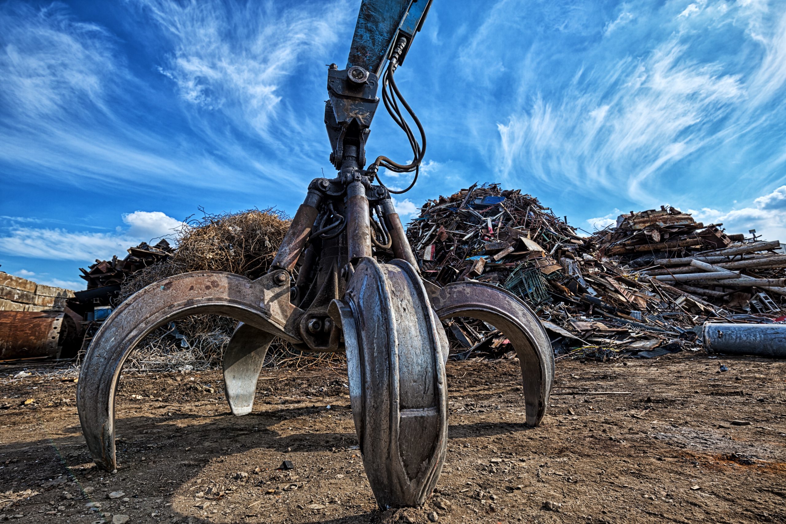 A gripper attached to an excavator with a pile of metal scrap in the background
