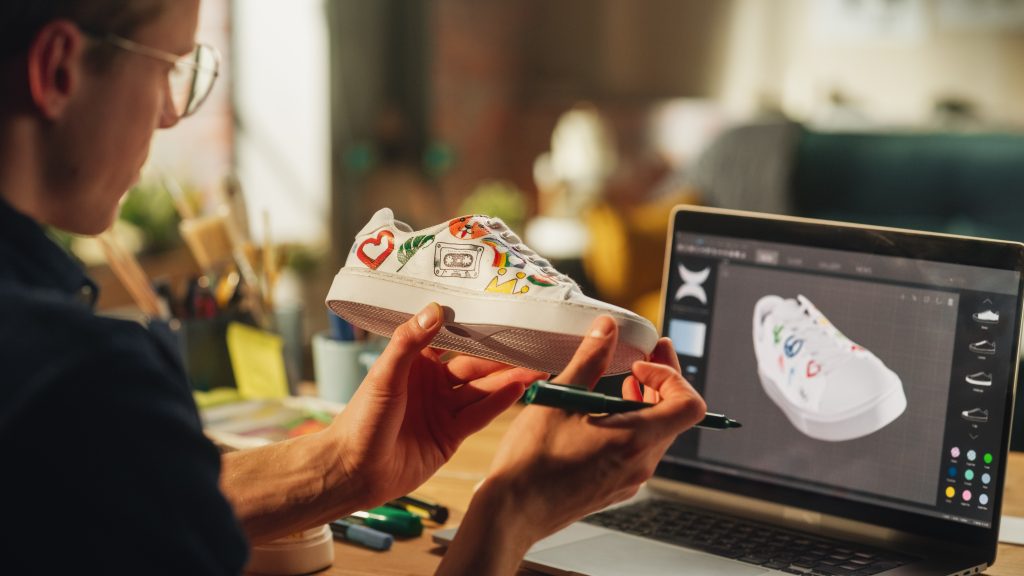 A worker looking at sketches on laptop and creating a custom-made shoes design