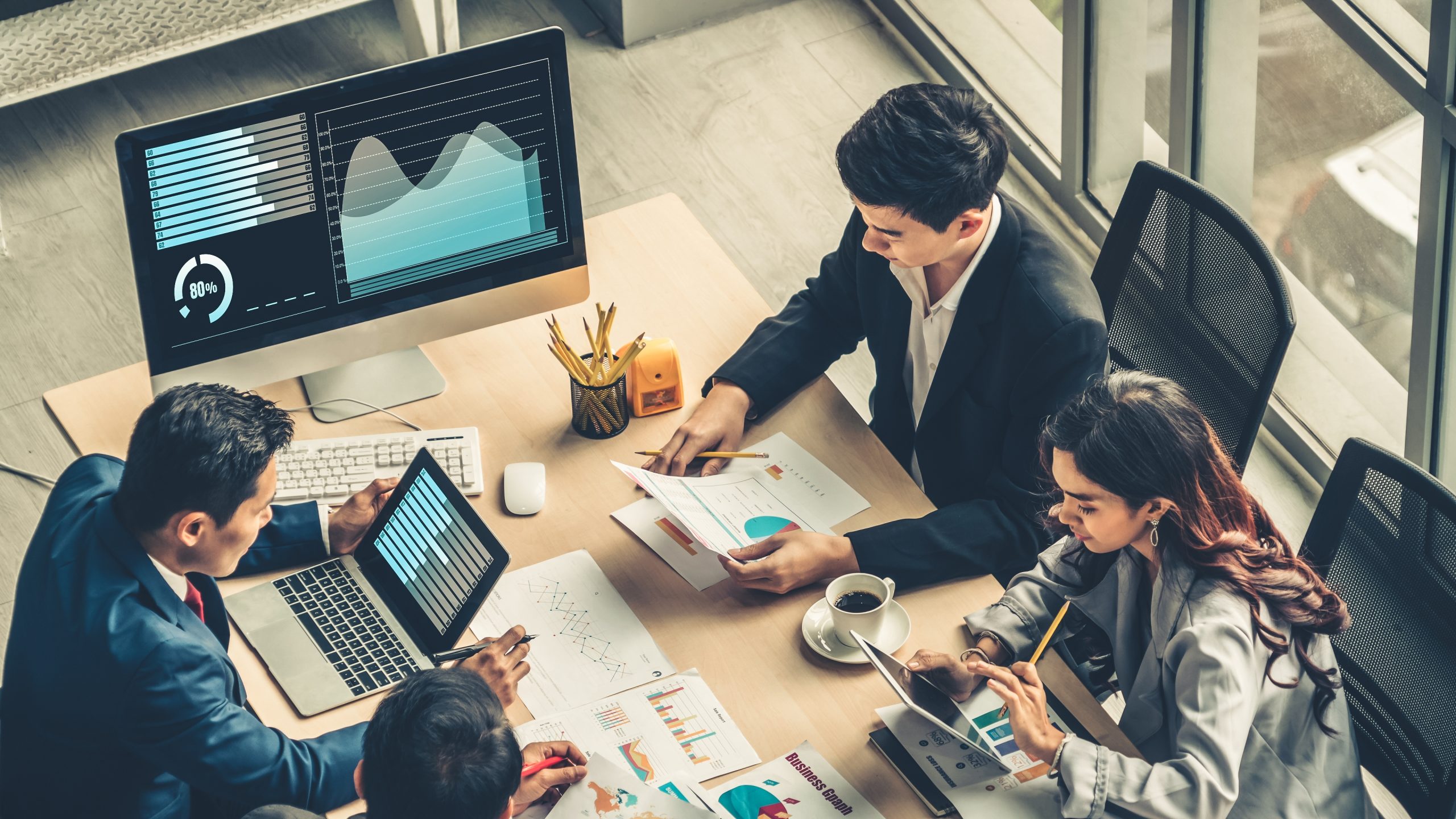 Employees sitting around a desk looking at documents showing charts