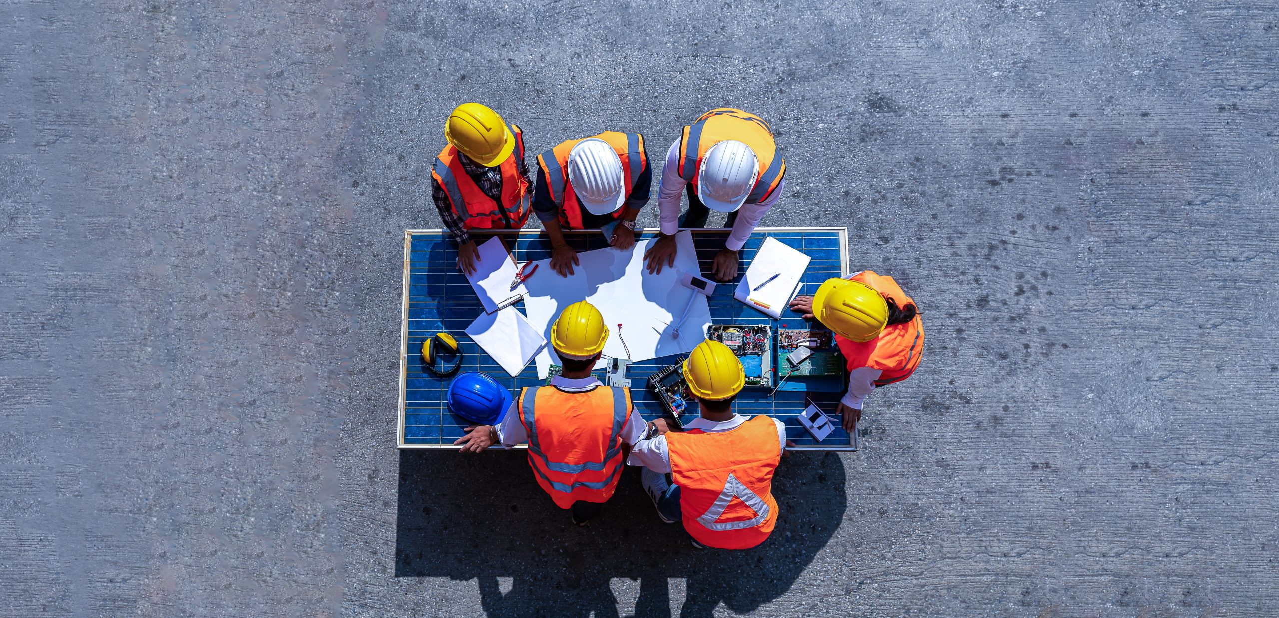 Top view of workers wearing safety gear around a table looking at the production plan