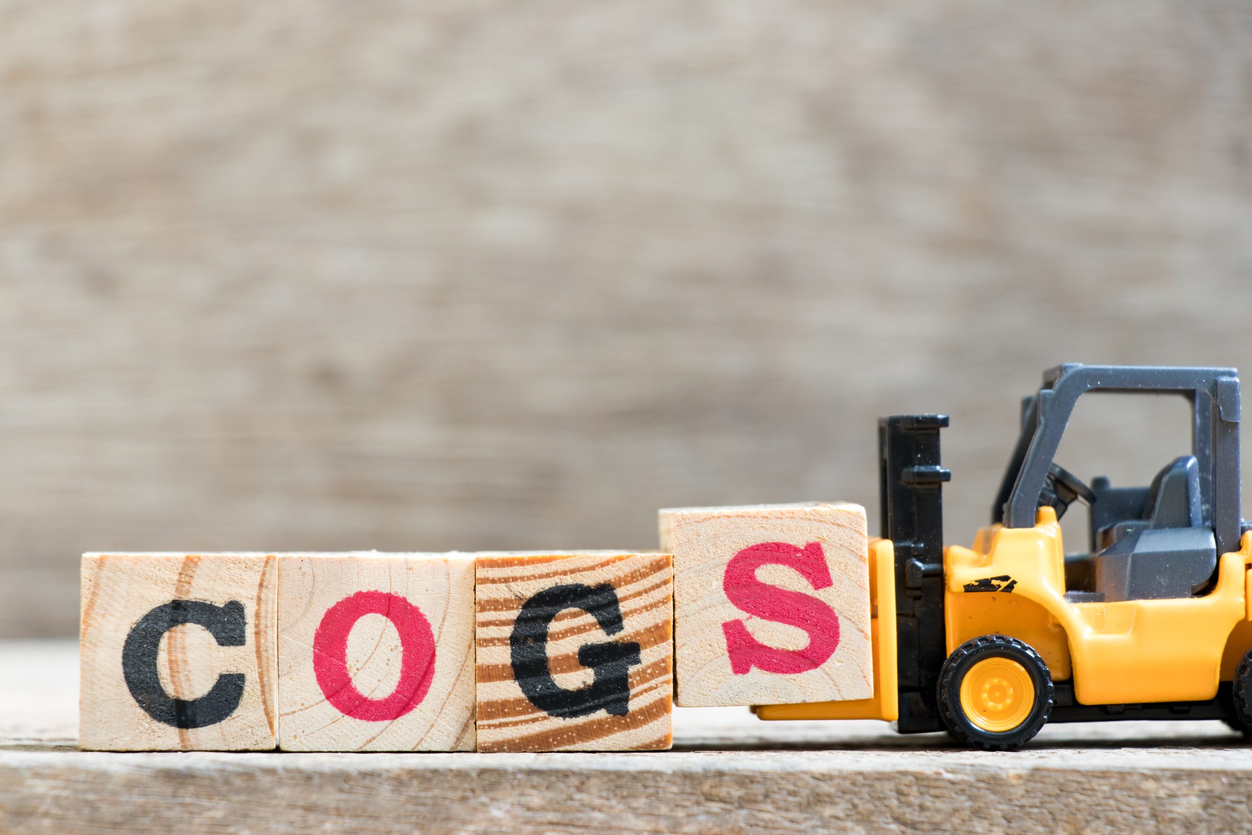 Model forklift lifting wooden blocks that spell out COGS