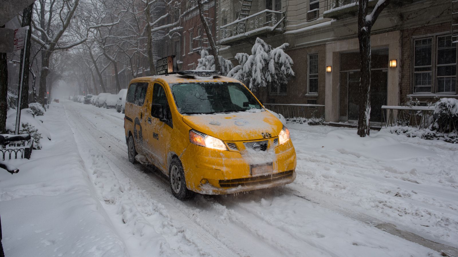 Yellow cab driving through snowy New York street.