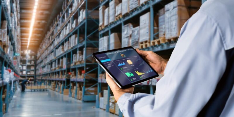 A worker holding a tablet in a warehouse full of inventory