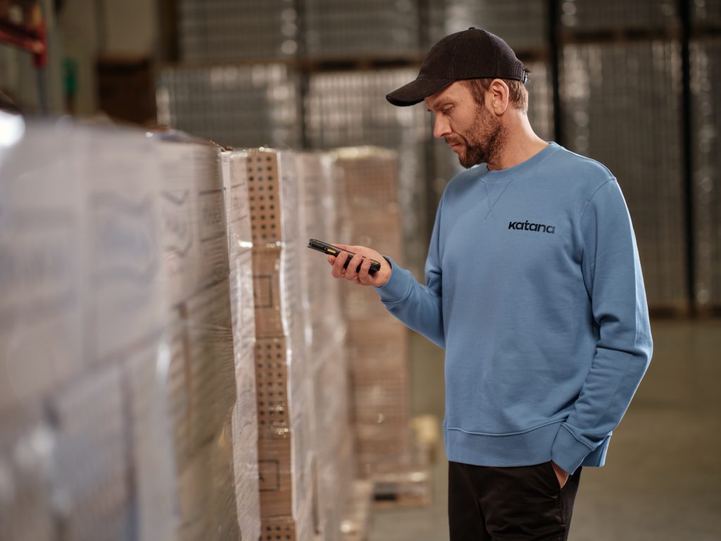 A worker in a warehouse holding a barcode scanner and checking inventory