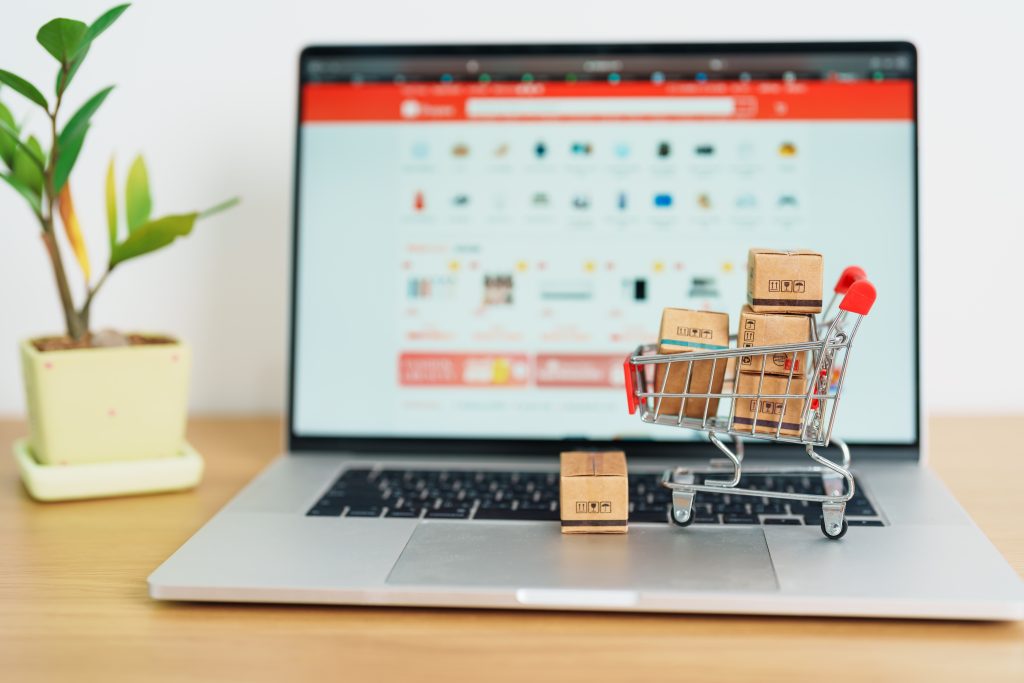 Tiny shopping cart overflowing with boxes on sitting on a laptop