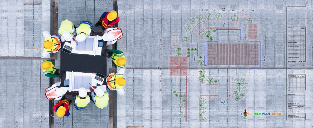 Top view of workers wearing PPE gathered around a table looking at warehouse layout plans